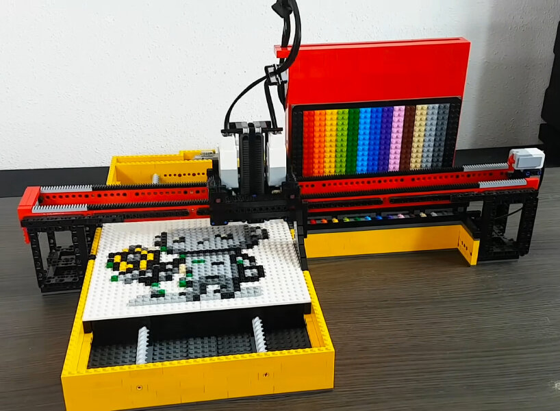 Photo of a robot printer made of LEGO bricks. It somewhat resembles a 3D printer, with a bed that moves back and forth, and an arm (that places 1x1 LEGO plates) that moves across the bed. A bank of 14 possible color options is also attached to this.