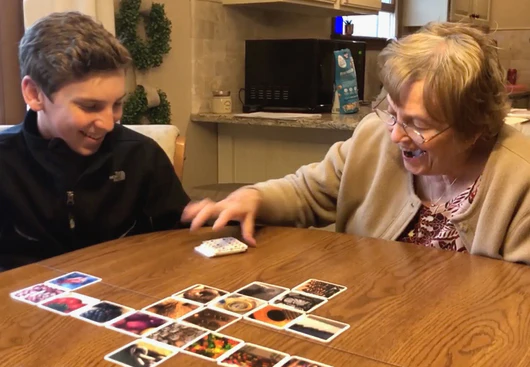 Photo of a young person playing a game of OuiSi with an elderly lady. 