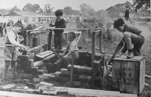 Black and white photo of several kids, working with wood, bricks, and various construction tools.