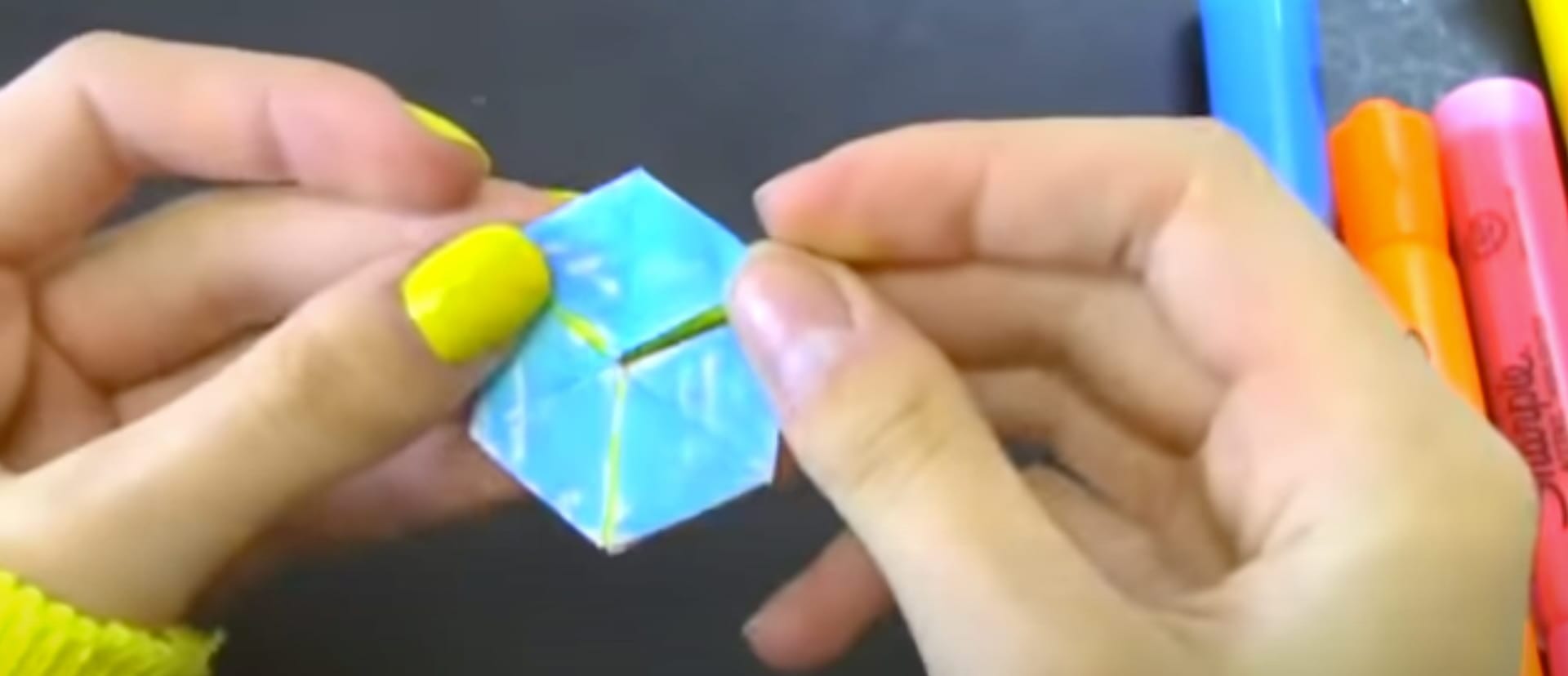 A pair of hands playing with paper contraption folded into a hexagon shape.