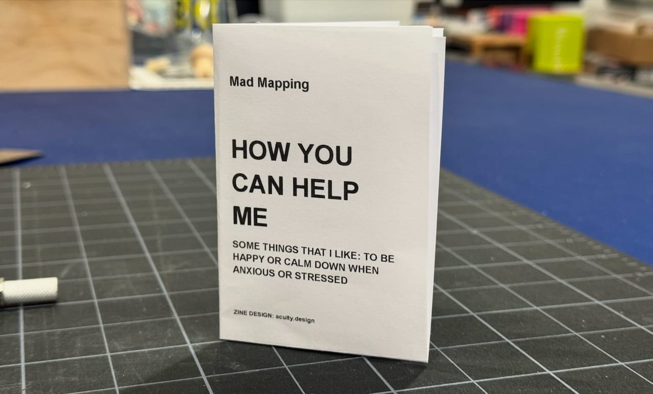 Photo of a hand-assembled black and white zine on a crafts table. Zine is titled "How you can help me."
