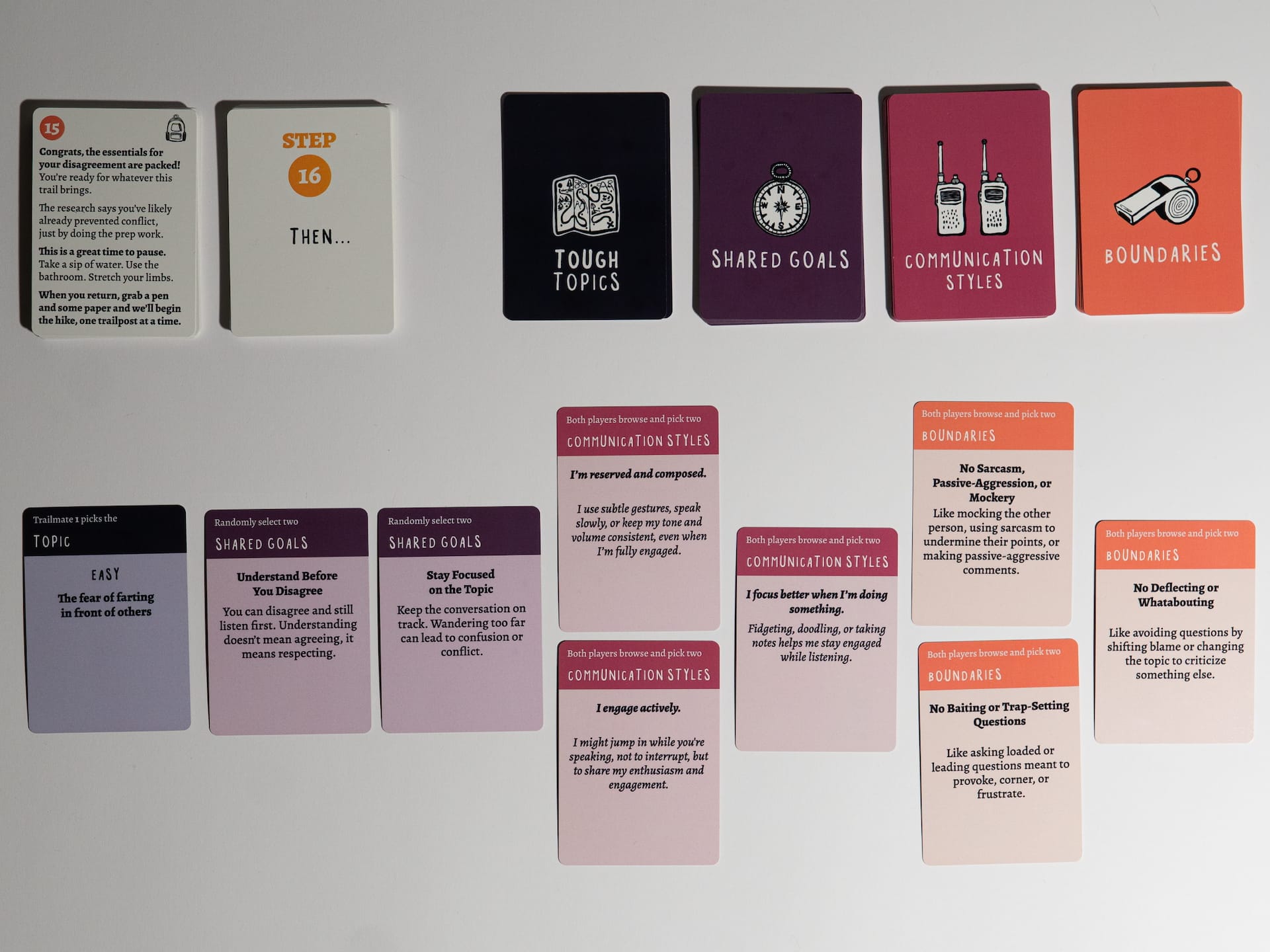 The Disagree Differently card game laid out on a table. Across the top: a step card (Step 16, “Then…”) beside four category decks — Tough Topics (black), Shared Goals (purple), Communication Styles (magenta), and Boundaries (orange), each with an icon (map, compass, walkie-talkies, whistle). Below, sample cards drawn from each: a Topic card (“Easy — the fear of farting in front of others”), a Shared Goals card (“Understand Before You Disagree”), Communication Styles cards (“I engage actively”), and Boundaries cards (“No Sarcasm, Passive-Aggression, or Mockery”).