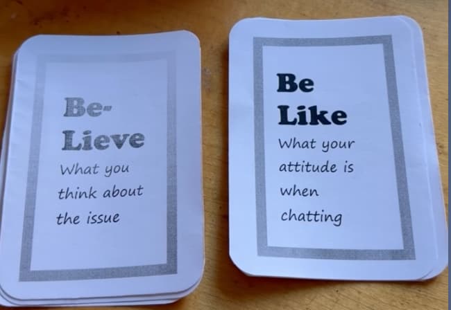 Two small printed decks on a wooden surface, each card bordered by a simple gray frame: a “Be-Lieve” deck (“What you think about the issue”) and a “Be Like” deck (“What your attitude is when chatting”).