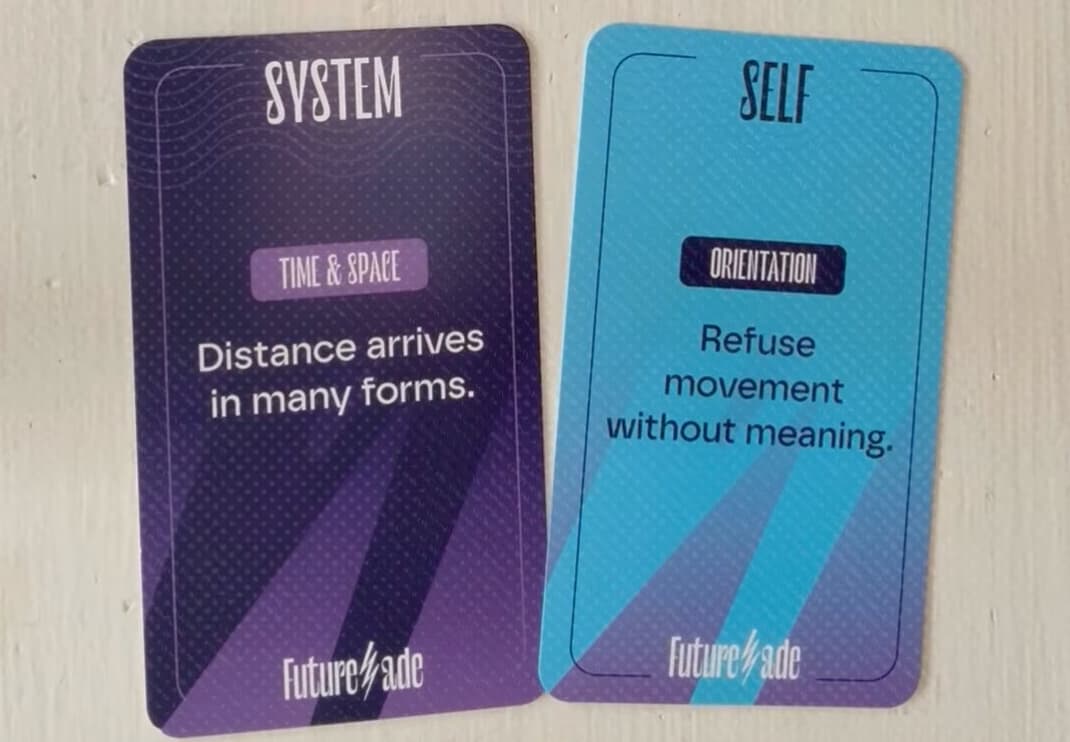 Two cards from the System & Self deck (Futur.ade) side by side: a purple “System” card labeled “Time & Space” reading “Distance arrives in many forms,” and a blue “Self” card labeled “Orientation” reading “Refuse movement without meaning.”